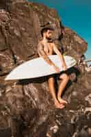 Free photo young man holding surf board near stones