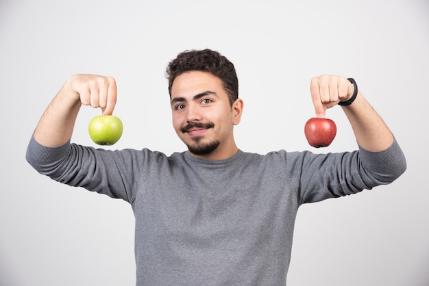 Young man holding two apples on gray.