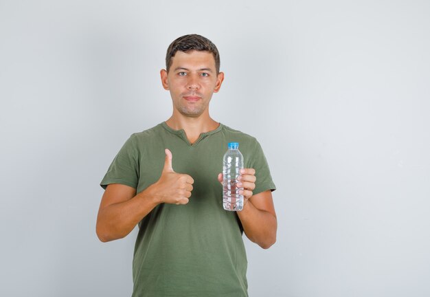 Young man holding water bottle and showing thumb up in army green t-shirt front view.