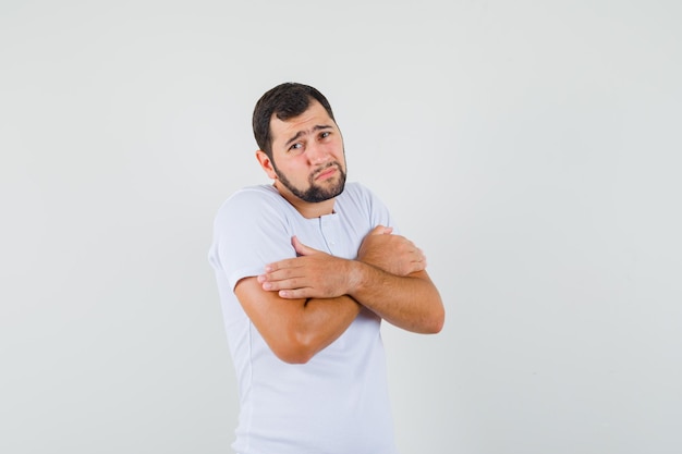 Young man hugging himself in t-shirt and looking cold. front view.