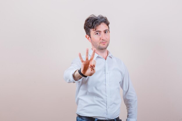 Young man indicating the number three in white shirt, jeans and looking confident