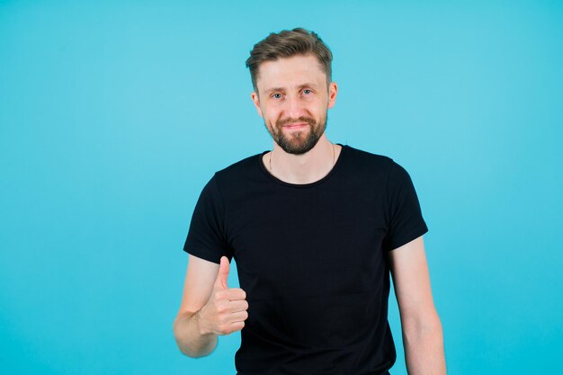 Young man is looking at camera by showing perfect gesture on blue background