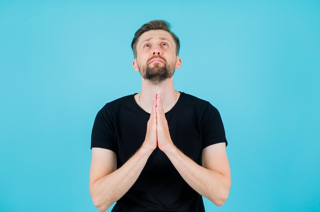 Free photo young man is looking up and praying by holding hands together on blue background