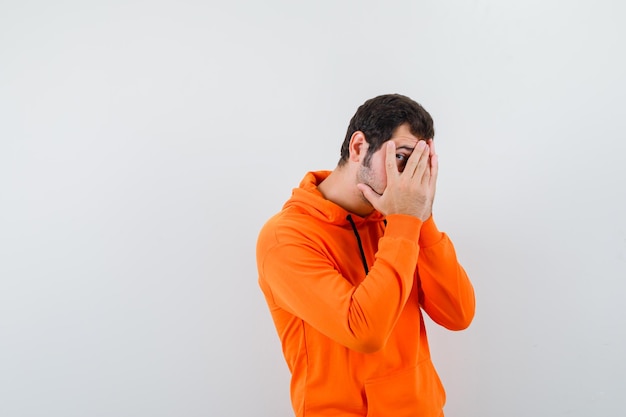 The young man is peeking through fingers on white background