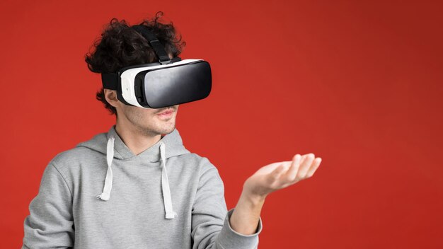 A young man is playing games using VR glasses holding a virtual thing red background