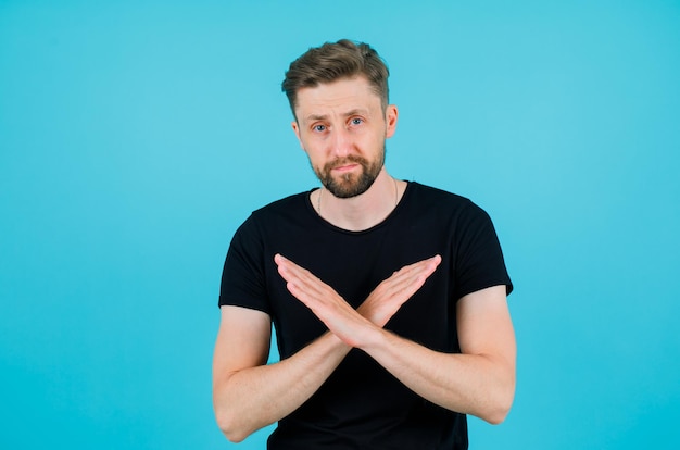 Free photo young man is showing enough gesture by crossing hands on blue background