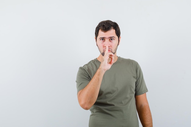 The young man is showing silent gesture by holding forefinger on lips  on white background