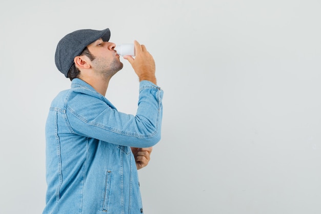 Young man in jacket,cap drinking from bottle of pills and looking hopeful space for text