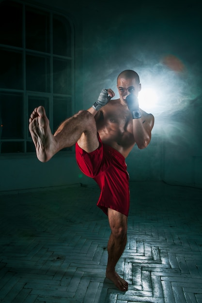 Free photo young man kickboxing in blue smoke