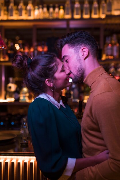 Young man kissing and embracing with woman near bar counter