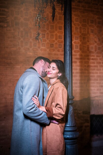 Young man kissing happy woman near street lamp