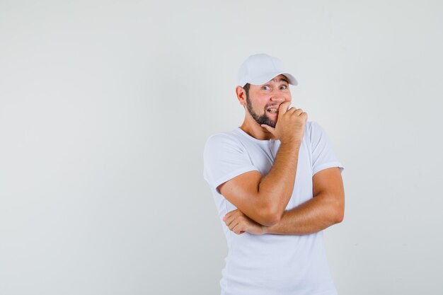 Young man laughing with hand in t-shirt,cap and looking merry , front view. space for text