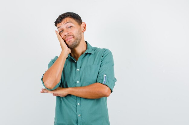 Young man leaning cheek on raised palm in shirt and looking cheerful