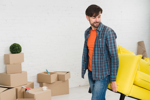 Young man lifting the yellow sofa in his new house