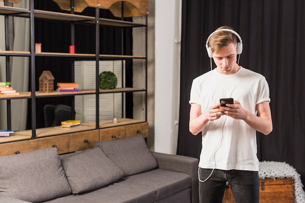 Free Photo young man listening music on headphone through mobile phone at home