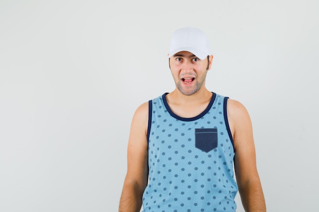 Free photo young man looking at camera in blue singlet, cap and looking cheerful