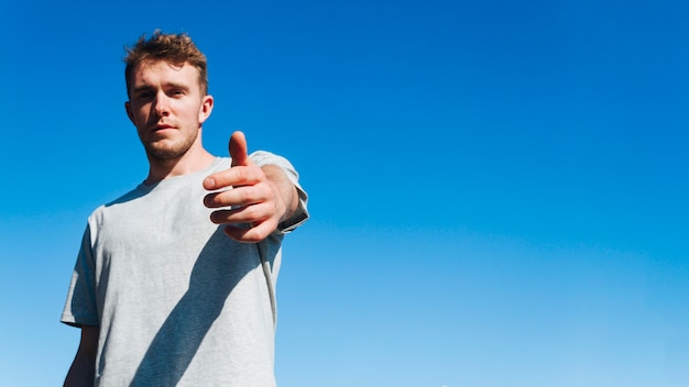 Free photo young man looking at camera and inviting someone against blue sky background