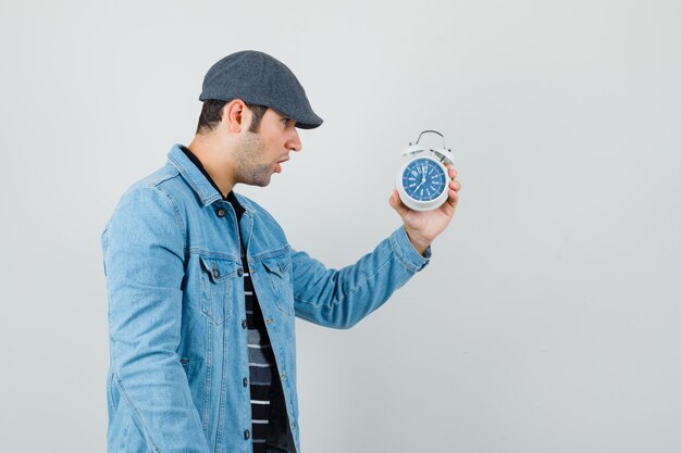 Young man looking at clock in jacket,cap and looking excited. .