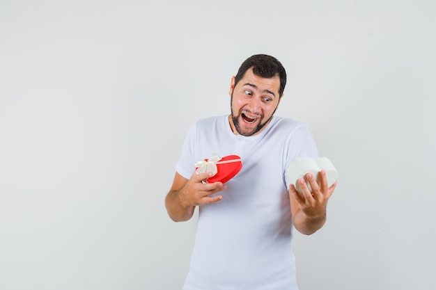 Young man looking into present box in white t-shirt and looking cheerful. front view. space for text