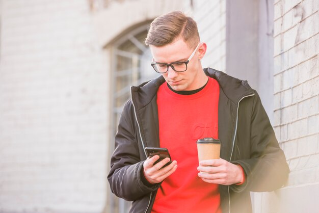 Young man looking at mobile phone holding disposable coffee cup in hand