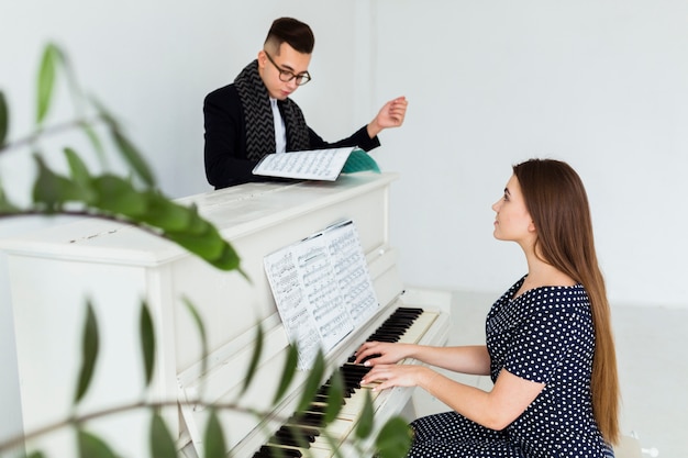 Young man looking at musical sheet assisting the woman playing piano