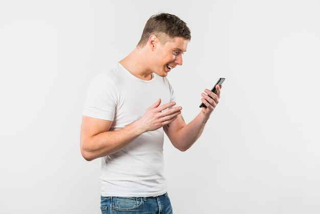 Free Photo young man looking at smartphone smiling against white backdrop