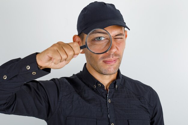 Young man looking through magnifying glass in black shirt with cap