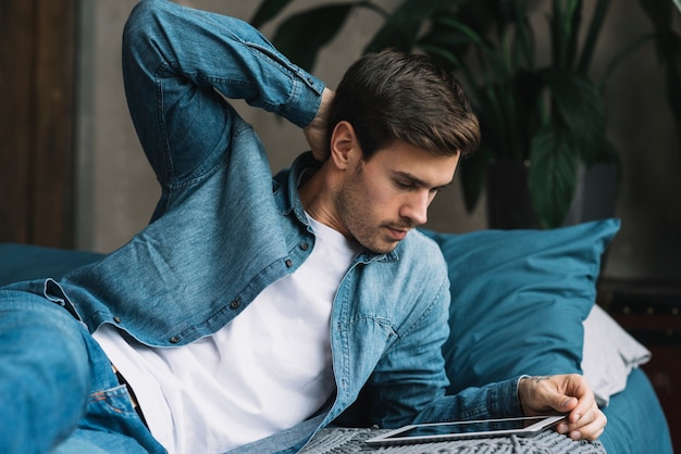 Young man lying on bed looking at digital tablet