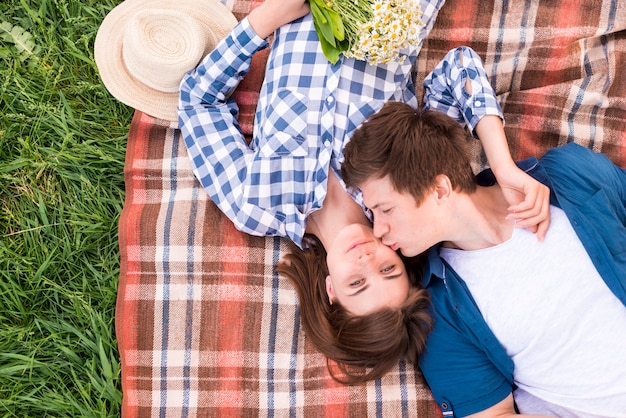 Free photo young man lying on blanket and kissing girlfriend on cheek