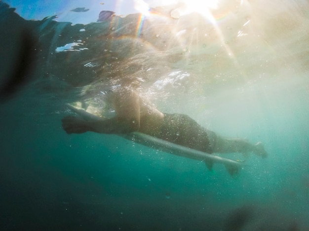 Young man lying on surfboard in blue water