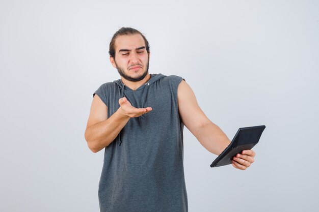 Young man making asking question gesture in hoodie and looking displeased, front view.