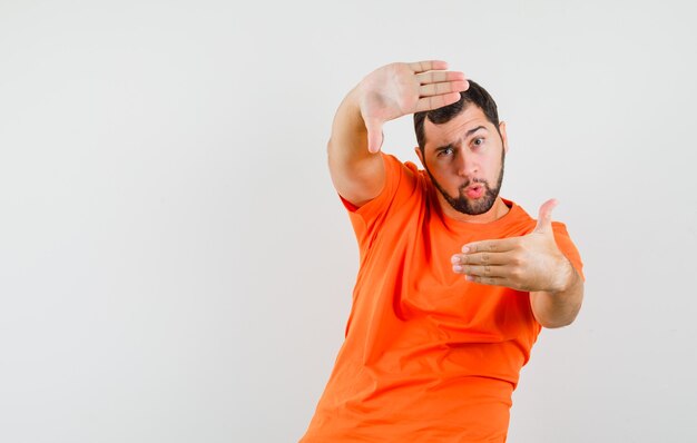 Young man making frame gesture in orange t-shirt and looking confident. front view.