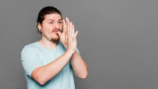 Young man making hand trumpet gesture against grey background