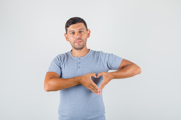 Young man making heart gesture with fingers in grey t-shirt