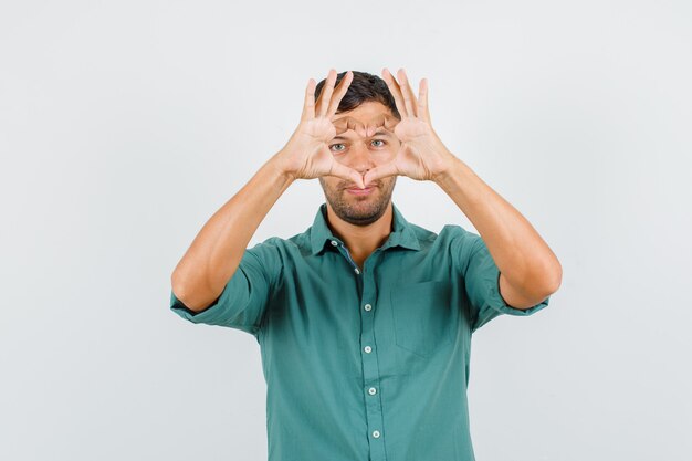 Young man making heart shape with hands in shirt and looking friendly.