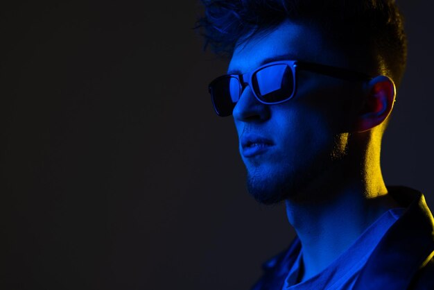 Young man model with smile in black fashionable leather jacket on colorful pink neon lights