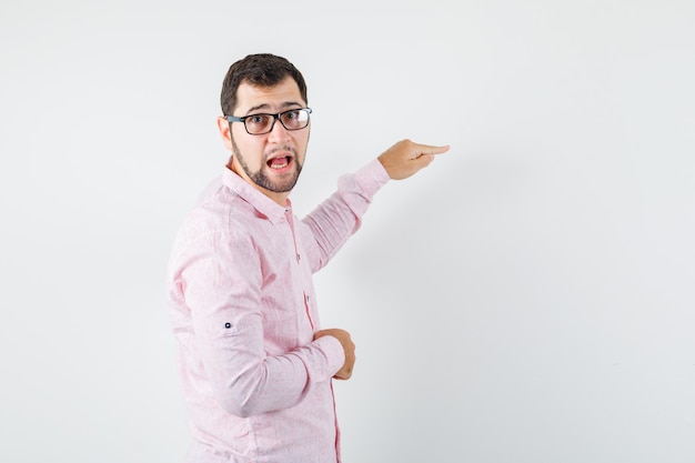 Young man in pink shirt pointing away and looking irresolute