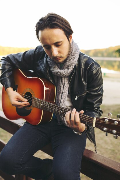 Young man playing on guitar at the lake