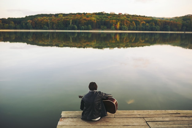 Free photo young man playing on guitar at the lake