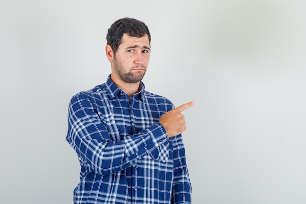 young man pointing away with finger in checked shirt and looking upset