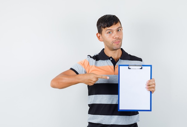 Young man pointing at clipboard in t-shirt and looking careful