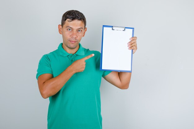 Young man pointing finger at clipboard in green t-shirt front view.