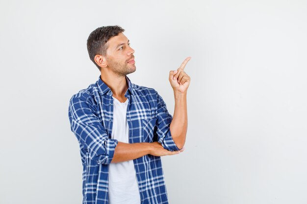 Young man pointing finger to side in shirt and looking focused. front view.