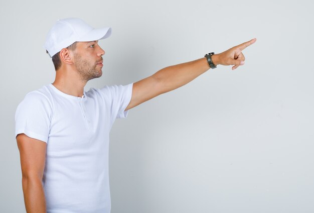 Free Photo young man pointing finger at something away in white t-shirt, cap .