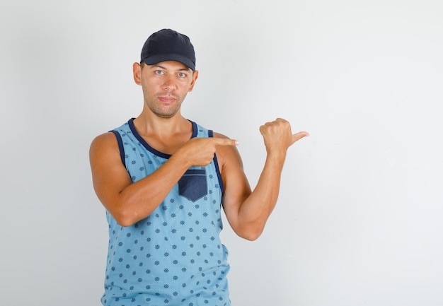 Young man pointing fingers away in blue singlet with cap