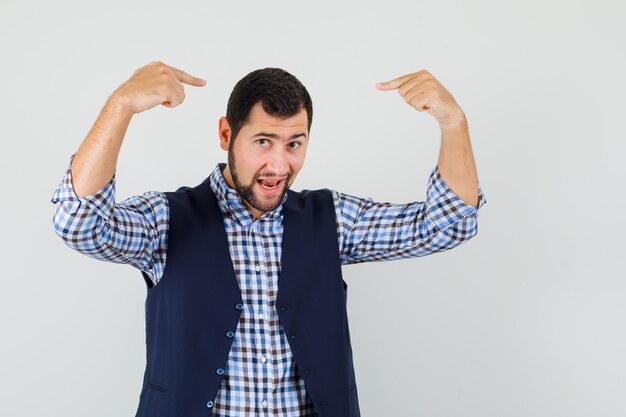 Young man pointing fingers at his head in shirt, vest and looking confident. front view.