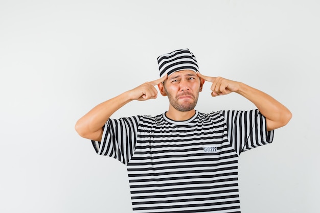 Young man pointing fingers at temples in striped t-shirt hat and looking sad  