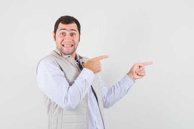 Young man pointing right with index fingers in beige jacket and looking optimistic. front view.