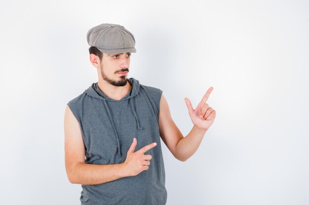 Free photo young man pointing up in gray t-shirt and cap and looking serious