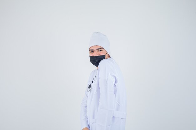 Young man posing while standing in white uniform, mask and looking cheerful .